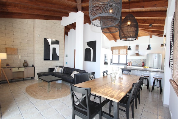 Cozinha moderna com ilha central, área de jantar com mesa de madeira e sala de estar com sofá de couro preto.