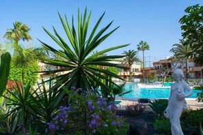 A swimming pool surrounded by tropical plants and a statue. - Casa Dan "Pool Views & Excellent Private Garden Terrace" (Corralejo)