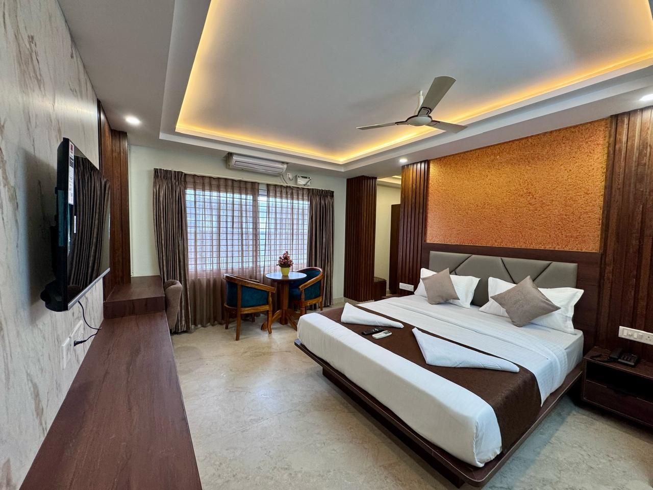 Habitación de hotel con una cama grande, un escritorio con dos sillas, un televisor y un ventilador de techo.
