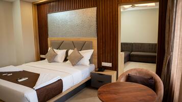Habitación de hotel con cama, mesita de noche, una mesa redonda de madera y un espejo que refleja una sala de estar.