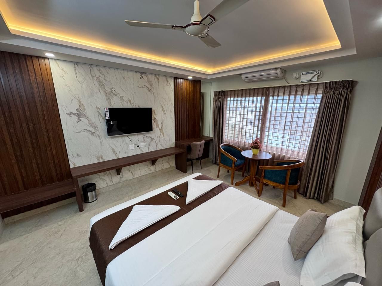 Una habitación de hotel con cama, escritorio, silla, televisor y ventilador de techo.