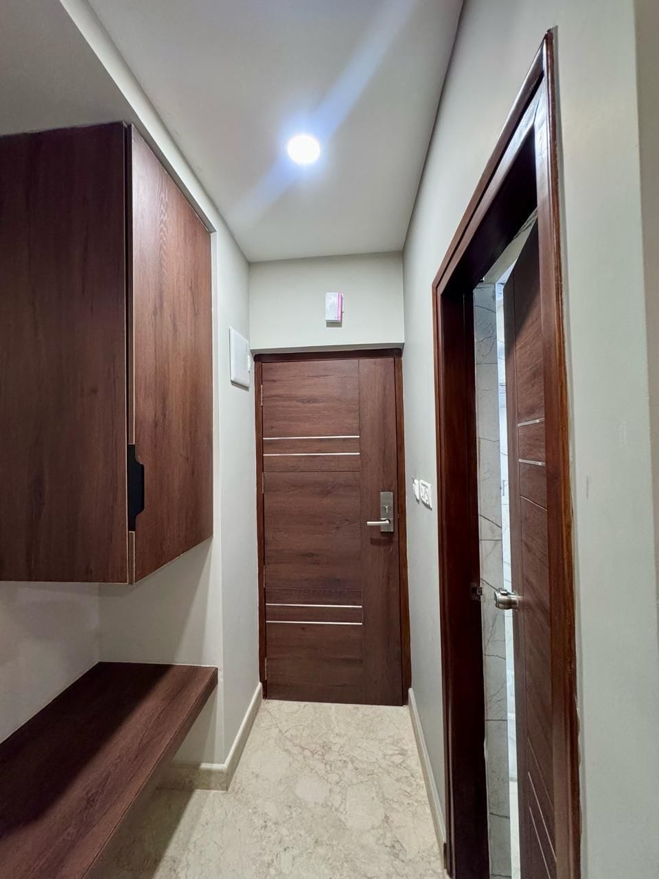 Un pasillo con una puerta de madera, un banco y una lámpara en el techo.