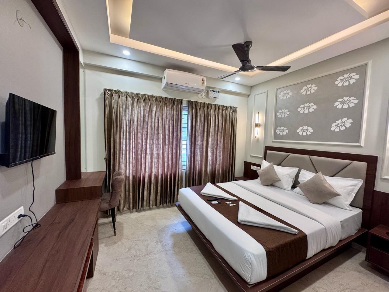 A hotel room with a bed, a desk, a chair, a ceiling fan, and an air conditioning unit.