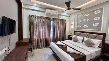 Una habitación de hotel con cama, escritorio, silla, ventilador de techo y aire acondicionado.