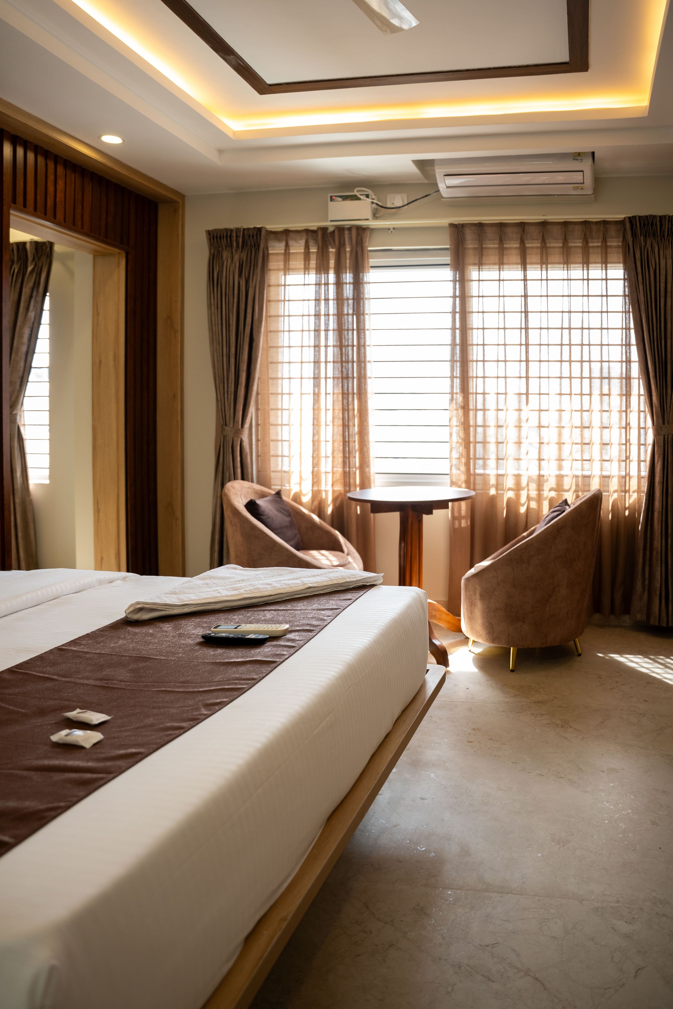 A hotel room with a bed, two armchairs, a small table, and a window with curtains.