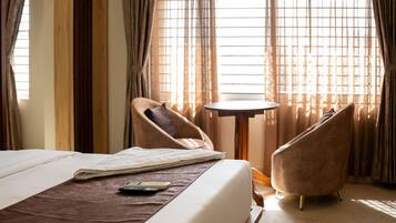 Habitación de hotel con una cama, dos sillones, una mesita y un ventanal con cortinas.