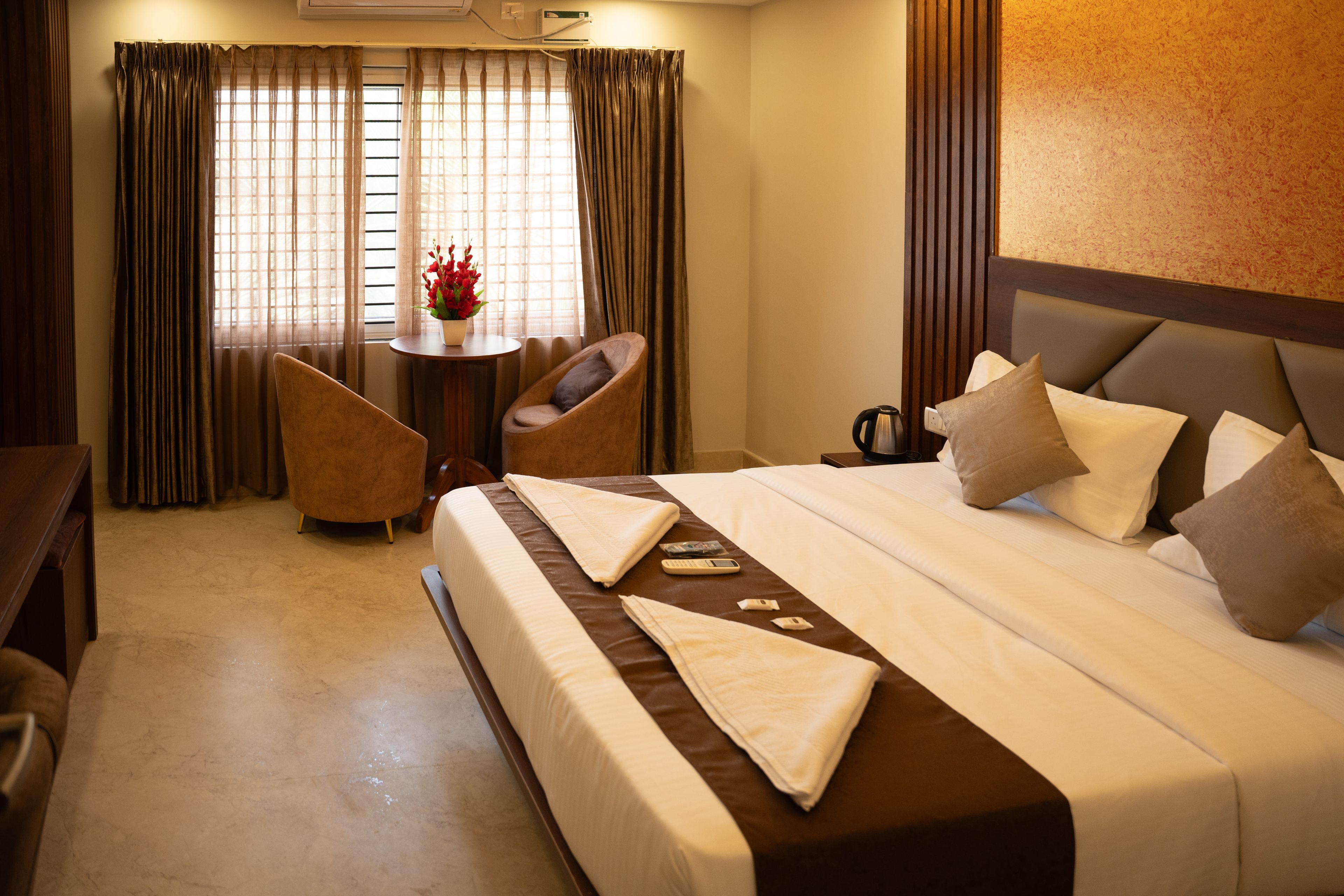 A hotel room with a bed, a desk, a chair, and a small table with a vase of flowers.