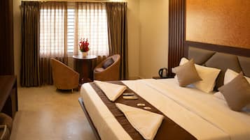 A hotel room with a bed, a desk, a chair, and a small table with a vase of flowers.