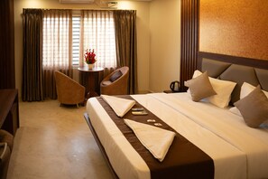 Habitación de hotel con cama, escritorio, silla y una pequeña mesa con un florero.