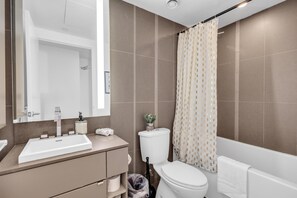 A bathroom with a sink, toilet, and shower curtain. - StayToronto - Downtown Peter Suites (Toronto)