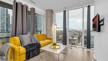 A modern living room with a yellow sofa, a coffee table, and a large window with a city view.