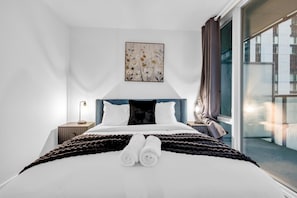 A modern hotel room with a large bed, a nightstand, a lamp, a window with curtains, and a wall-mounted artwork. - StayToronto - Downtown Peter Suites (Toronto)