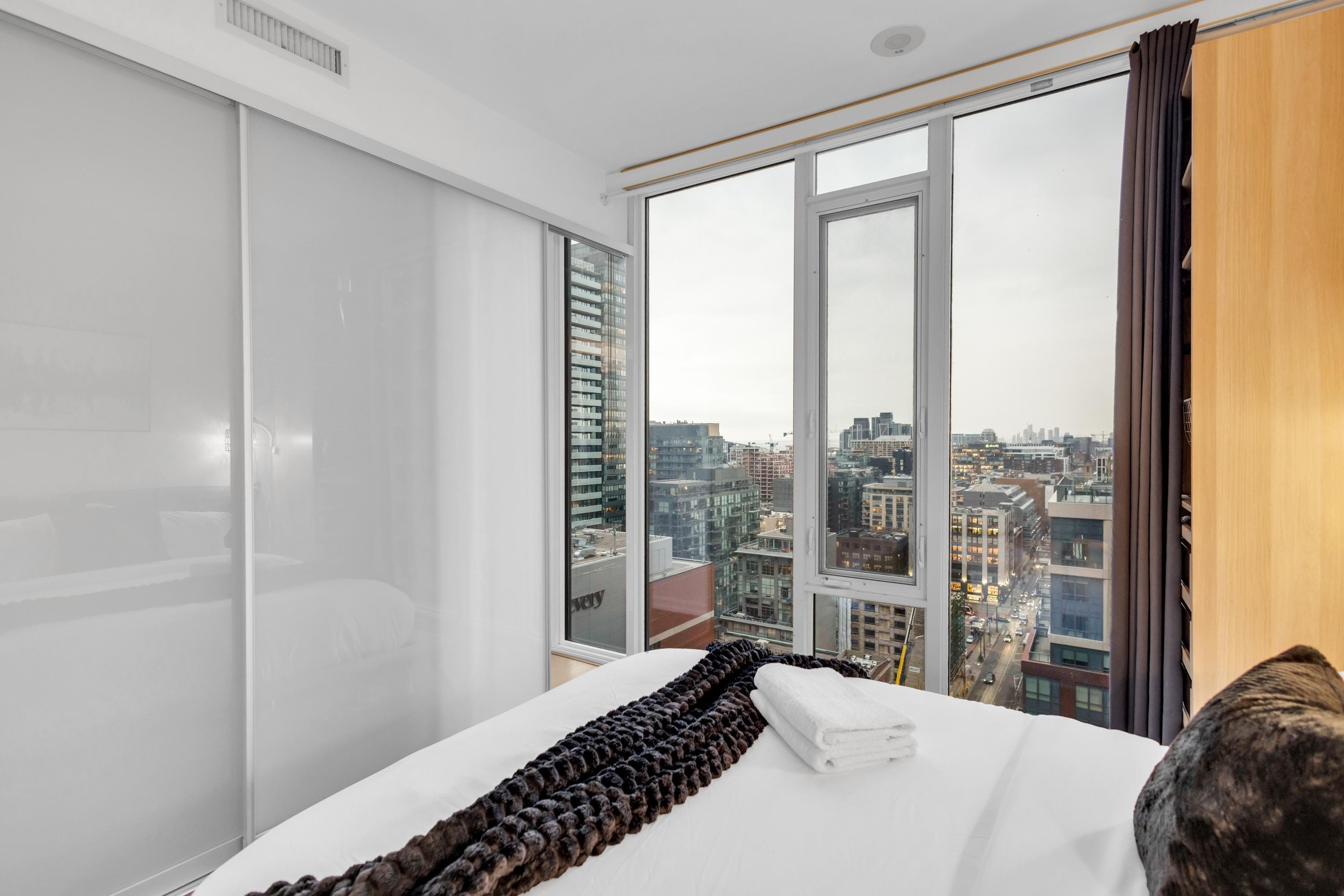 Habitación de hotel con una cama grande, vistas de la ciudad a través de ventanas del suelo al techo y una puerta corredera.