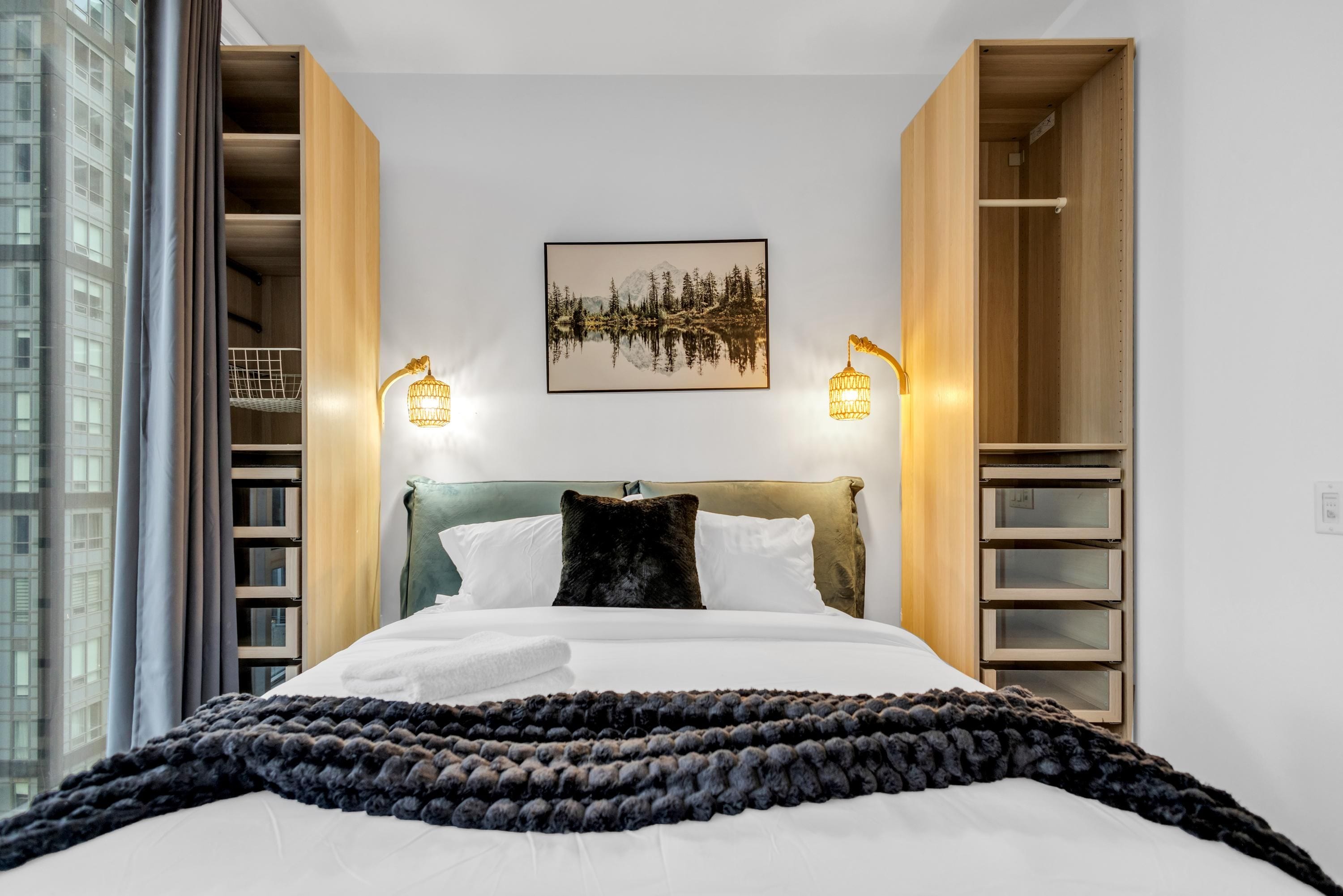 Una habitación de hotel con cama, cabecera, un cuadro colgado en la pared y dos apliques.