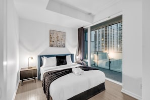A modern hotel room with a large bed, a bedside table, a nightstand, a window with a view of buildings, and a ceiling light. - StayToronto - Downtown Peter Suites (Toronto)