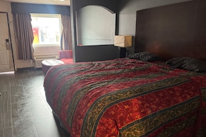 Ein Hotelzimmer mit einem großen Bett, einem roten Sessel, einem Fenster mit Vorhängen und einer Wandlampe.