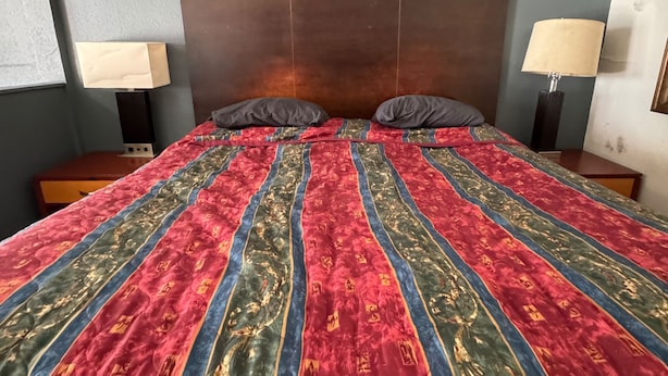 Ein Bett mit einem gemusterten Überwurf, zwei Kissen, einem Holzkopfende und Nachttischlampen.