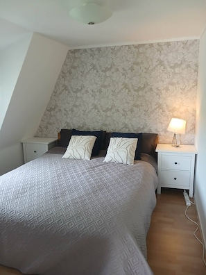 Un dormitorio con cama, dos mesitas de noche, una lámpara y un papel tapiz estampado.