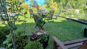 A garden with a table and chairs, surrounded by various plants and flowers.