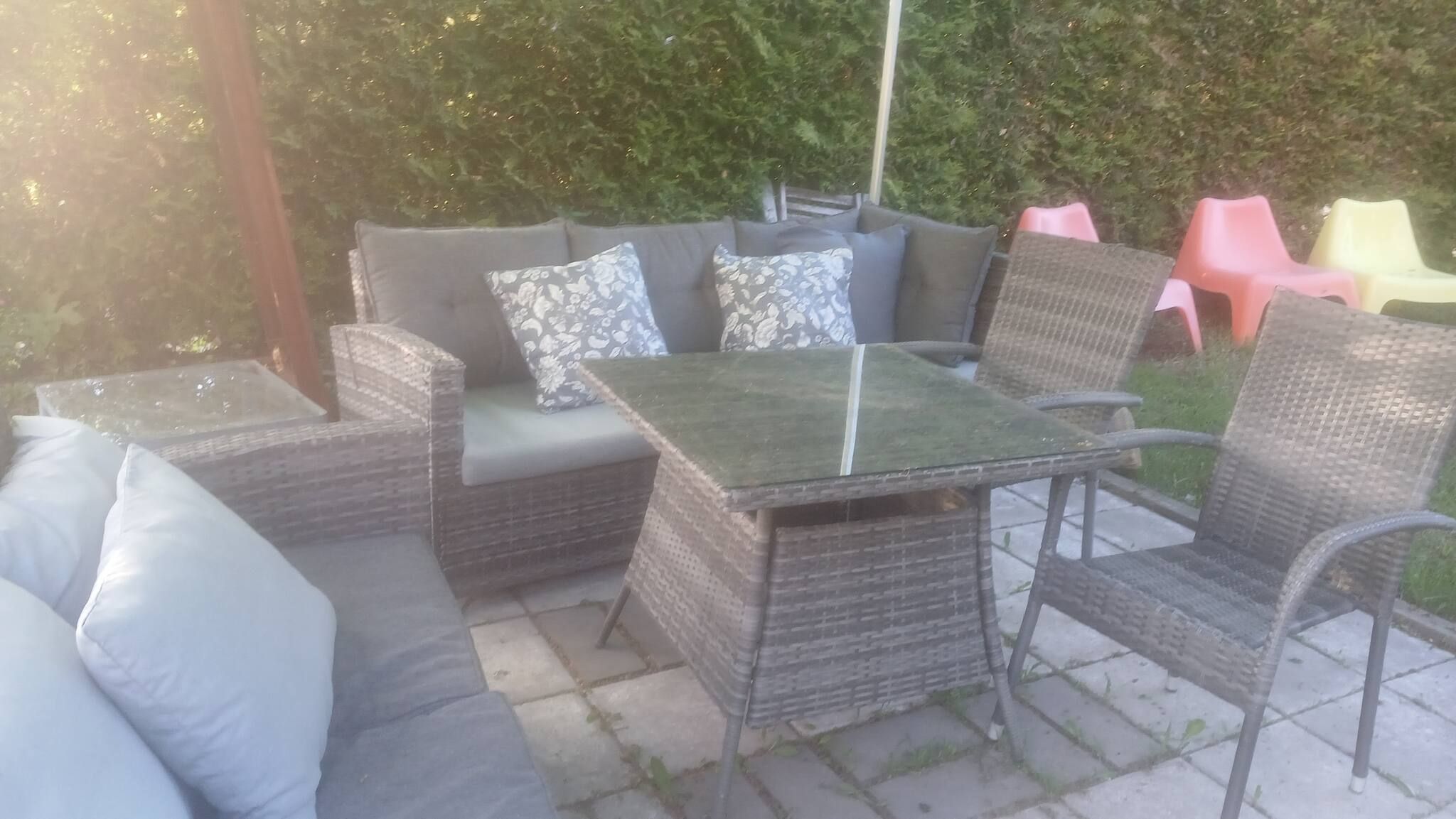 En udendørs terrasse med fletmøbler, herunder en sofa og stole, samt et bord med glasplade.