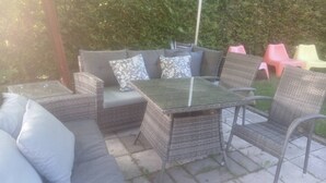 An outdoor patio with wicker furniture, including a sofa and chairs, and a glass-top table. - Charming Countryside Apartment Near Koping - Pet Friendly! (Köping)