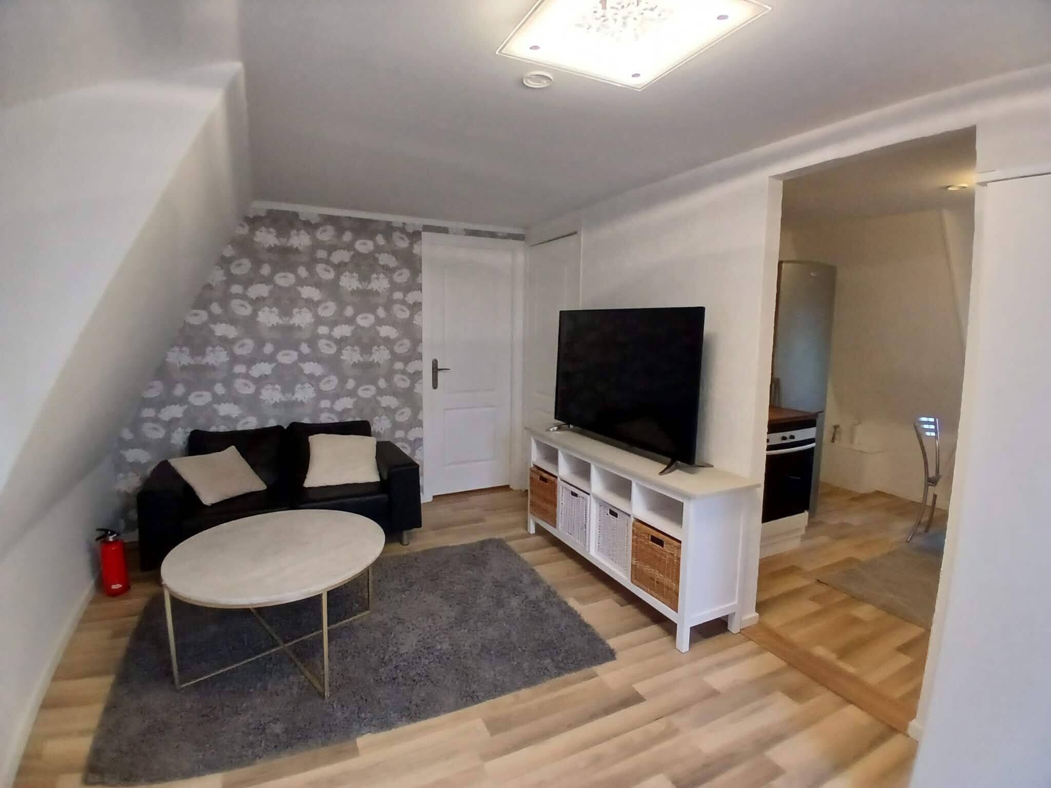 A small living room with a sofa, a television, a coffee table, and a patterned wall.