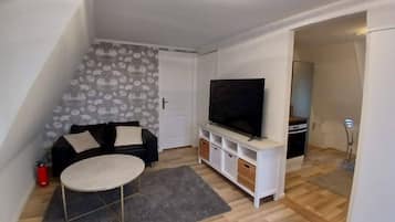 A small living room with a sofa, a television, a coffee table, and a patterned wall.