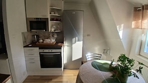 A compact kitchen with a microwave, oven, and refrigerator. There is a dining area with a table and chairs, and a potted plant on the windowsill.