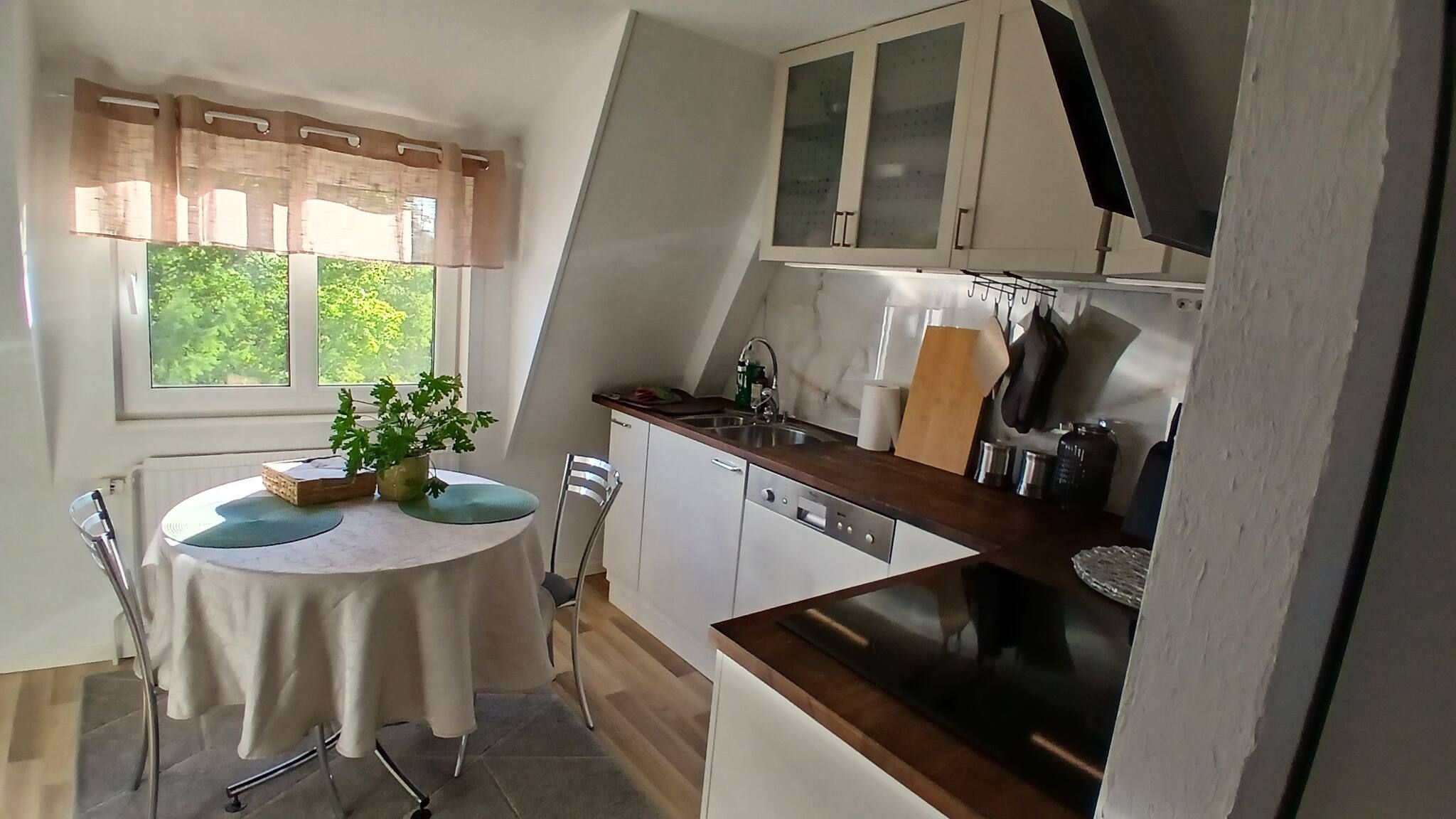 Eine kompakte Küche mit Essbereich, inklusive einem Tisch mit Pflanze, einem Fenster mit Vorhängen und einem Einbauofen.