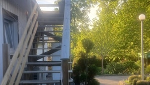 A building with a staircase leading to a covered area, surrounded by greenery and a paved path. - Charming Countryside Apartment Near Koping - Pet Friendly! (Köping)