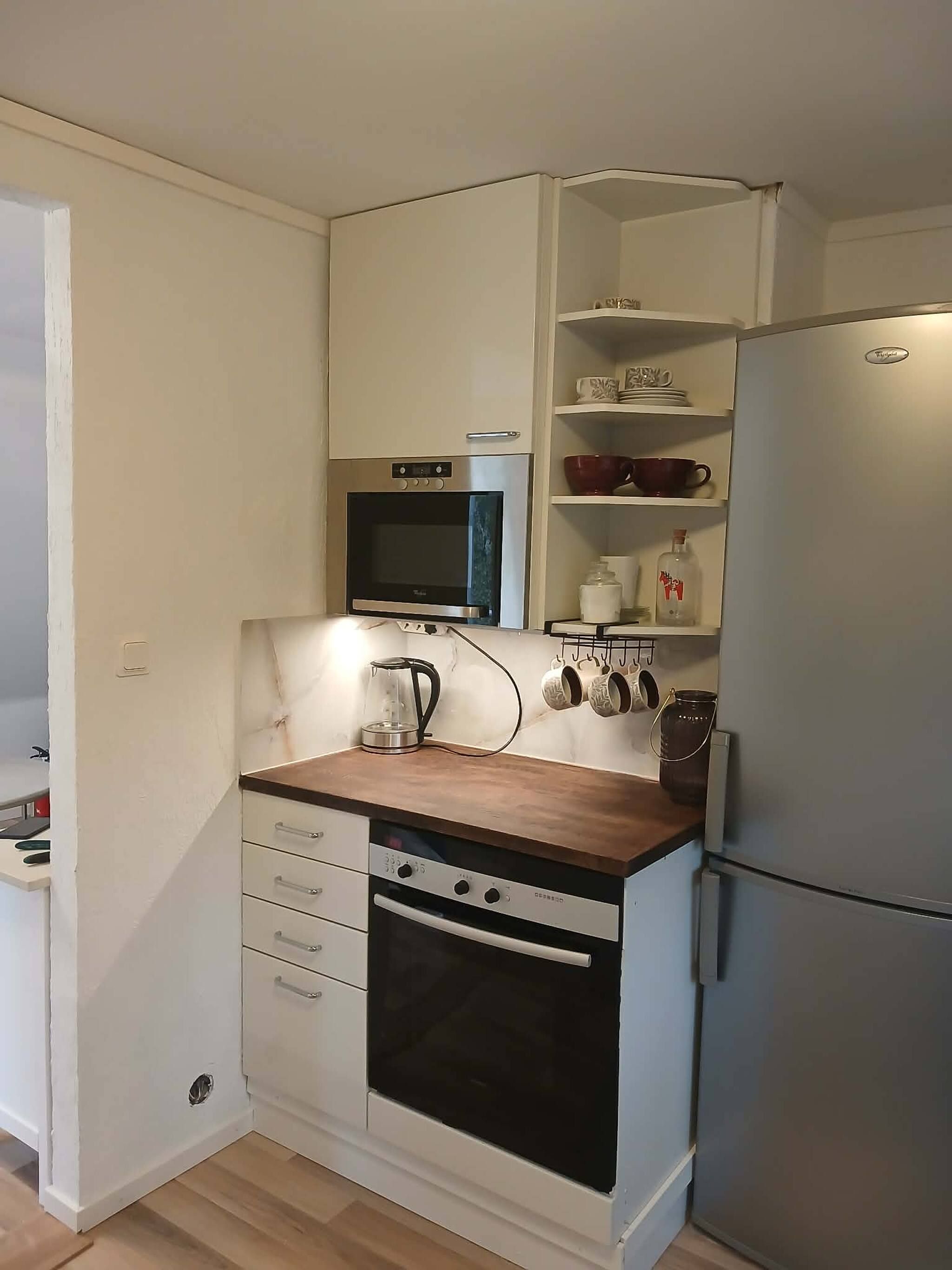 Eine kleine Küche mit Mikrowelle, Backofen und Kühlschrank.