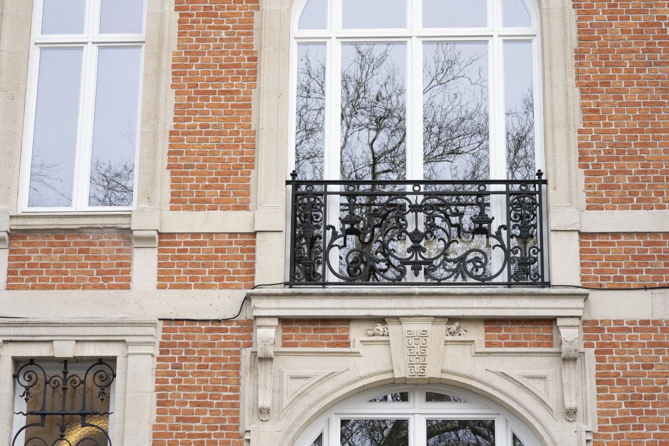 Une façade d’immeuble avec un revêtement en briques, de grandes fenêtres et des éléments décoratifs en fer forgé sur le balcon.