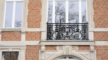 Une façade d’immeuble avec un revêtement en briques, de grandes fenêtres et des éléments décoratifs en fer forgé sur le balcon.