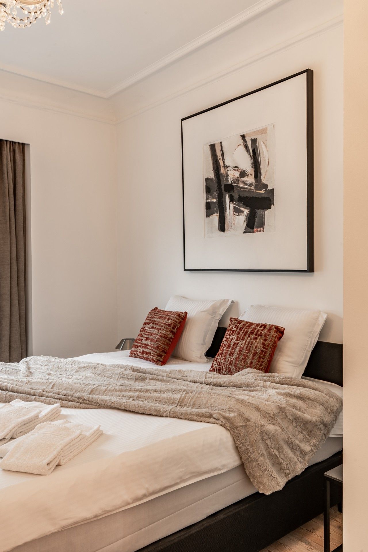 Une chambre à coucher moderne avec un lit, des oreillers, une couverture et un tableau abstrait encadré accroché au mur.