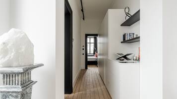 Un couloir doté d’un piédestal en marbre, d’un plancher en bois, de murs blancs et d’une porte donnant sur une autre pièce.