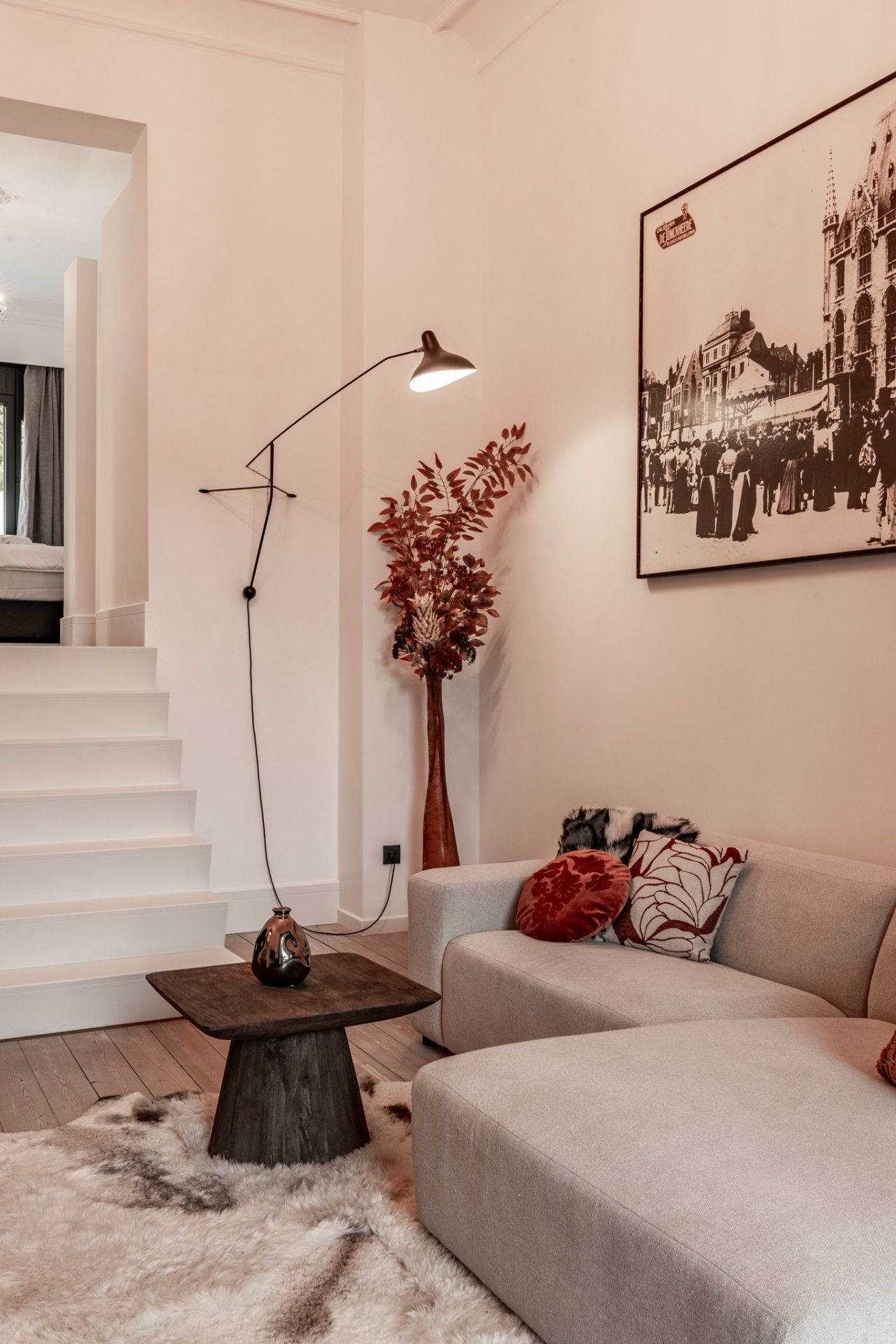 Un salon moderne avec un escalier, un grand lampadaire, une plante décorative, un canapé avec des coussins et un tableau encadré au mur.