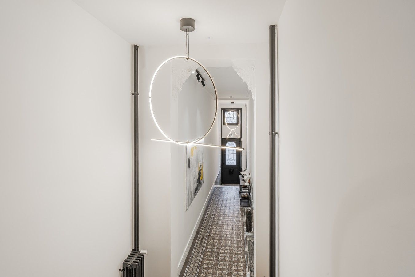 Un couloir doté d’un luminaire moderne, d’un radiateur et d’un sol à motifs, qui mène à une porte avec une fenêtre.