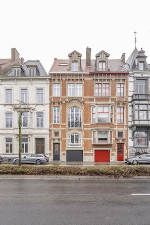 A row of three-story townhouses with a central garage door, a tree in front, and cars parked on the street. - Boutique Townhouse Suite | Bruges Centre (Brugge)