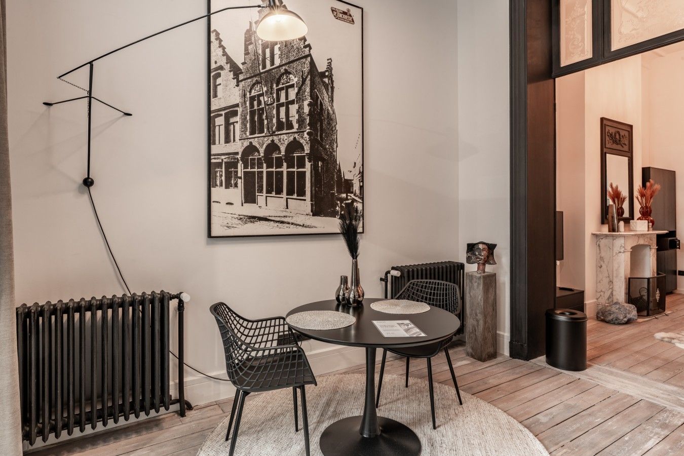 Un coin repas comprenant une table ronde, des chaises, un radiateur noir et un luminaire fixé au mur.