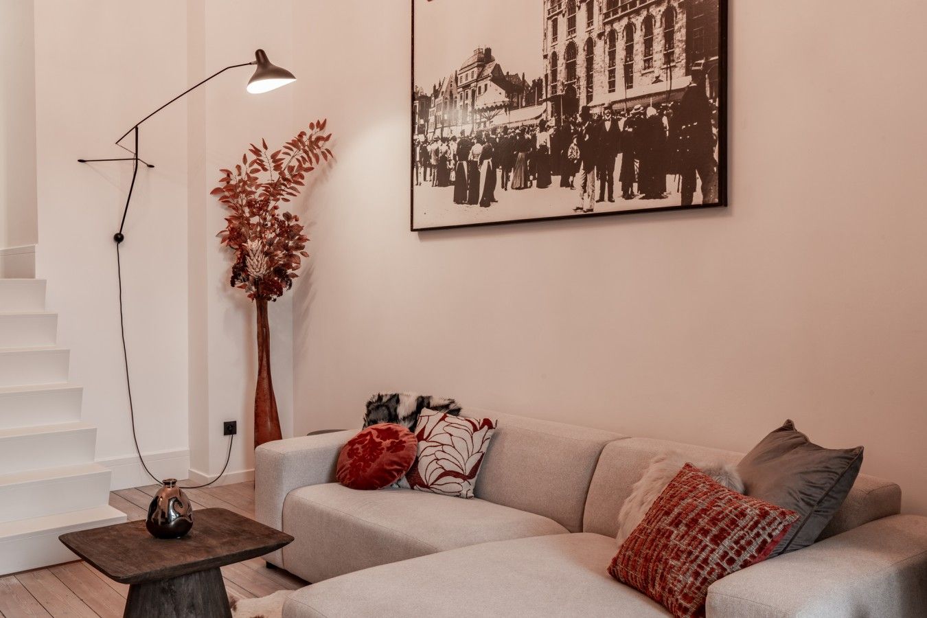 Un salon moderne avec un canapé, une lampe sur pied, un vase et une photographie encadrée accrochée au mur.