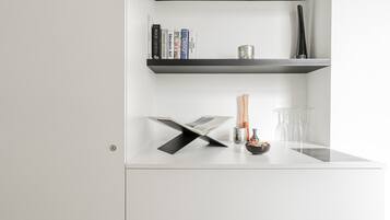 Une pièce moderne et minimaliste, avec un bureau blanc, une étagère noire contenant des livres, un vase et un pichet en verre.