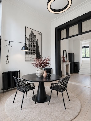 A dining area with a round table, two chairs, a vase with flowers, a black pendant light, and a framed picture on the wall. - Boutique Townhouse Suite | Bruges Centre (Brugge)