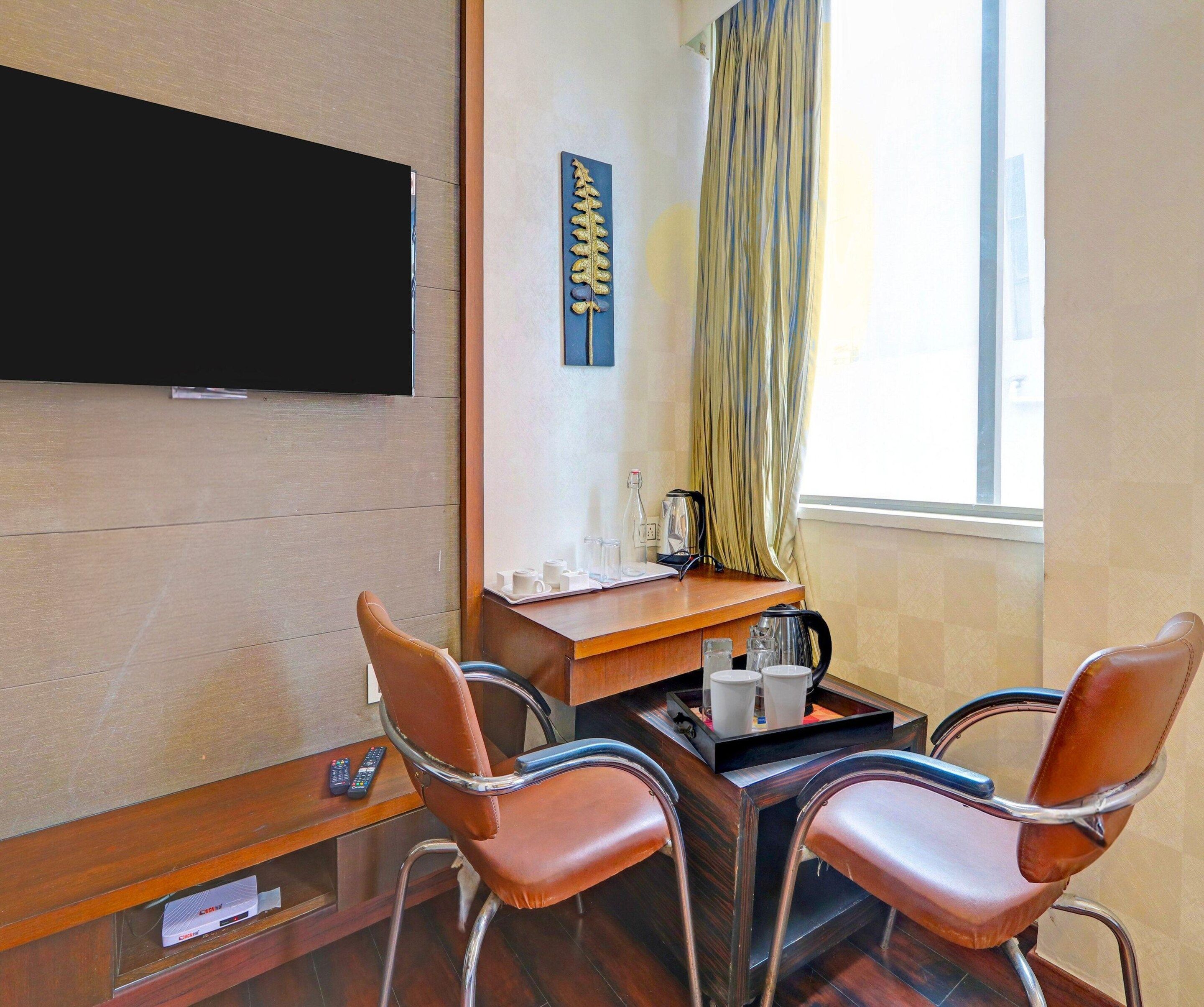 Habitació d'hotel amb televisió de pantalla plana penjada a la paret, una taula petita amb una cafetera, dues cadires de cuir i una finestra amb cortines.