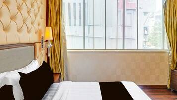 Habitació d'hotel amb un llit, una tauleta de nit, una làmpada i una finestra amb cortines.