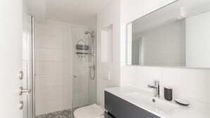 Ein modernes Badezimmer mit einer Duschkabine aus Glas, einer weißen Toilette, einem schwarzen Waschtisch mit Spiegel und einem gemusterten Boden.
