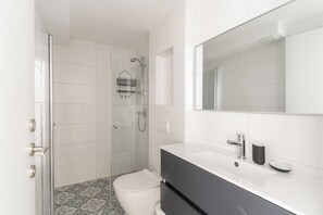 A modern bathroom with a glass shower enclosure, a white toilet, a black vanity with a mirror, and a patterned floor. - Blueground Florentine Bright Apartments (Tel Aviv-Yafo)