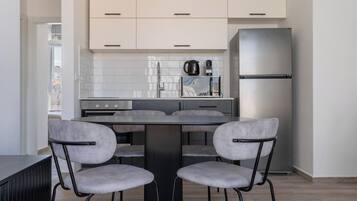 Une cuisine moderne avec une table à manger, quatre chaises, un réfrigérateur et une bouilloire posée sur le plan de travail.