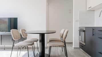 Een moderne keuken met een ronde eettafel en stoelen, een inbouwoven en een witte betegelde spatwand.