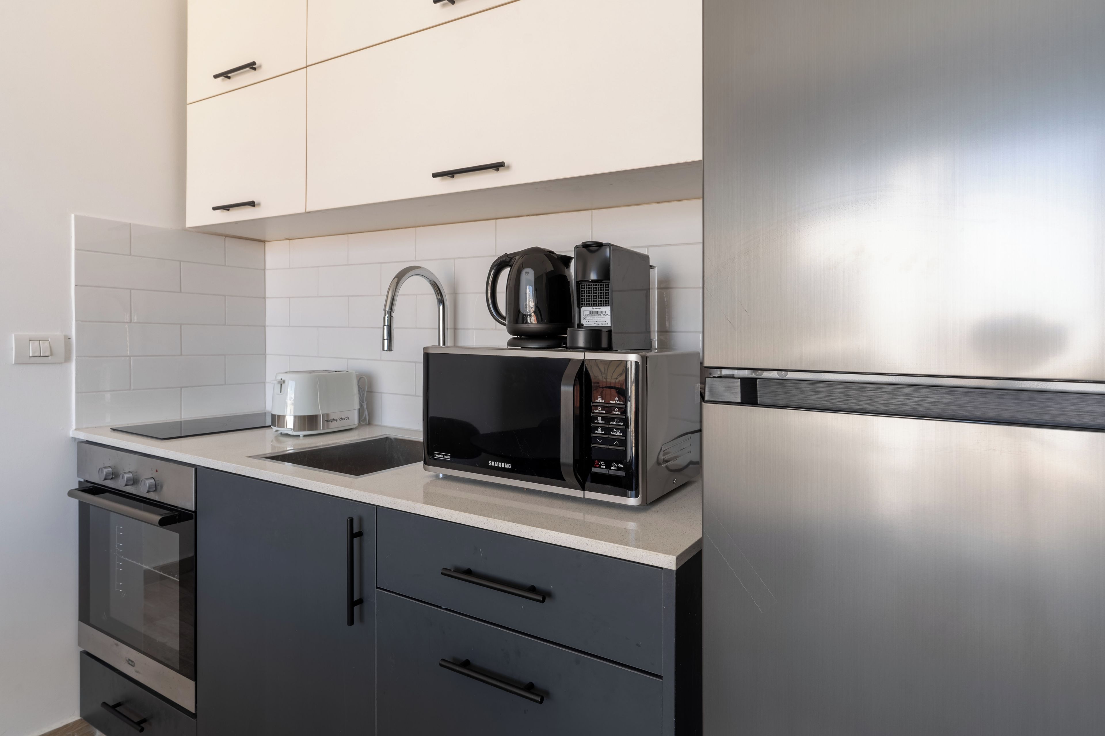 Eine moderne Küche mit einem Edelstahl-Kühlschrank, einer Mikrowelle, einem Wasserkocher und einem Toaster.