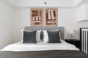 A bedroom with a bed, two pillows, a bedside table with a lamp, and two abstract paintings on the wall. - Blueground Florentine Bright Apartments (Tel Aviv-Yafo)